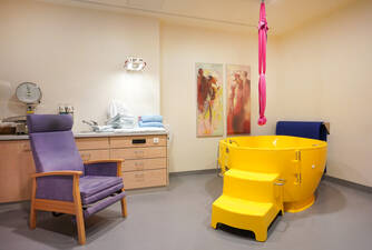 Bild eines Kreisssaals mit einer gelben, großen Badewanne rechts und einem lila Sessel links