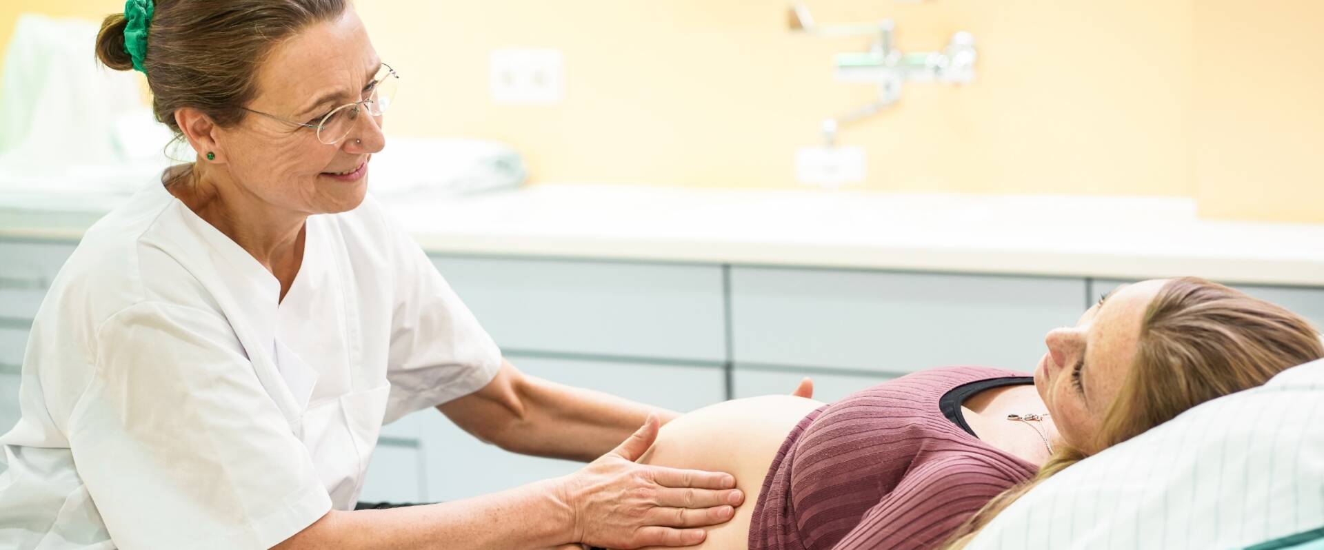 Hebamme tastet behutsam Bauch einer Hochschwangeren ab