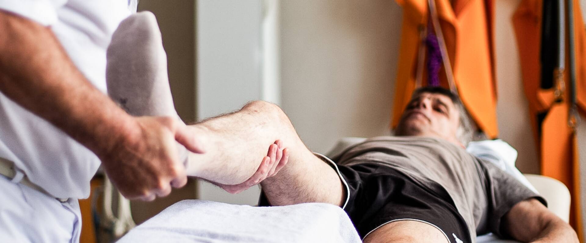 Physiotherapeut macht Übung am Bein mit einem liegenden Patienten
