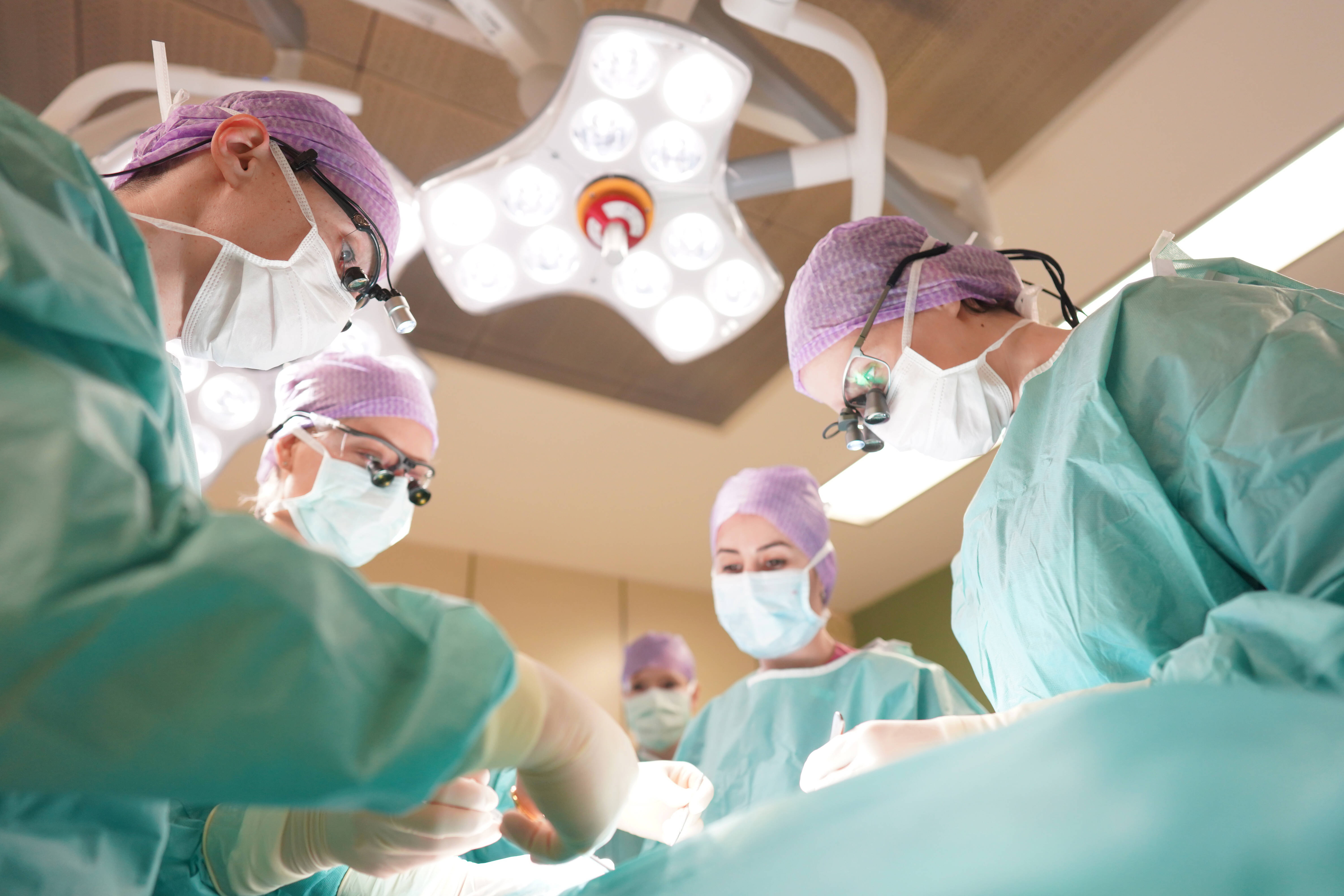 Das Team der Ästhetisch-Plastischen Chirurgie bei einer Operationmit türkisfarbenen OP-Kitteln und lila OP-Hauben und weißen Masken