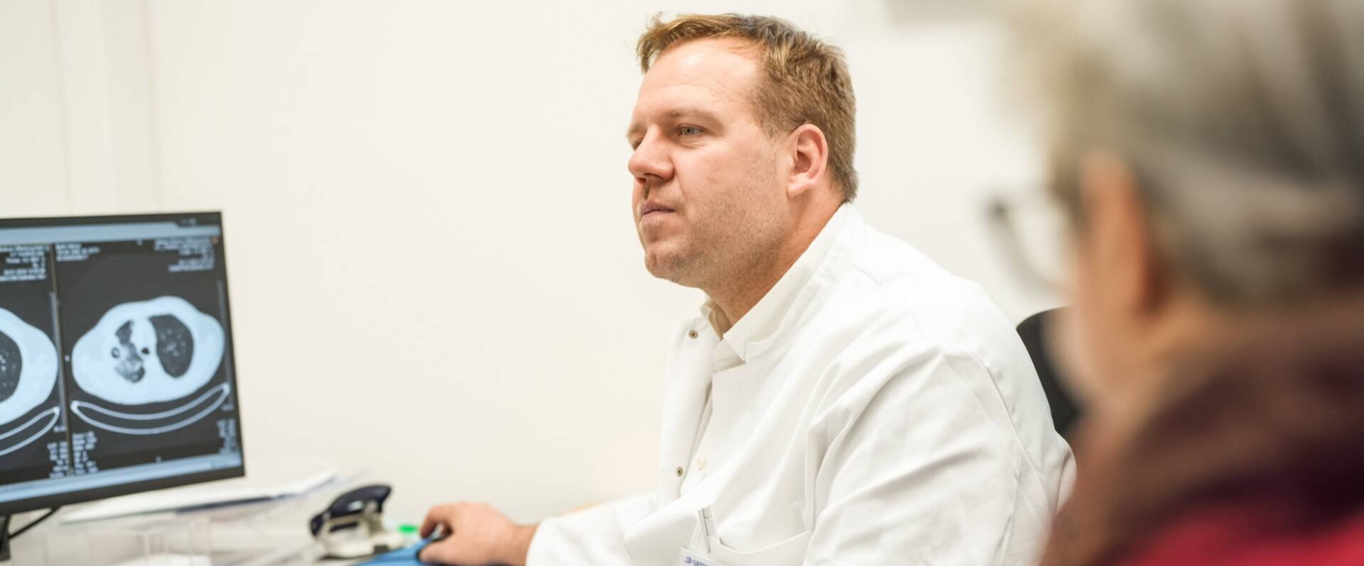 Arzt von einem Monitor mit MRT-Bild sitzend, einer Patientin etwas erklärend